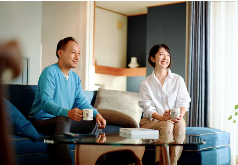 日差しが差し込むリビングで、青いソファに座る男性と女性。