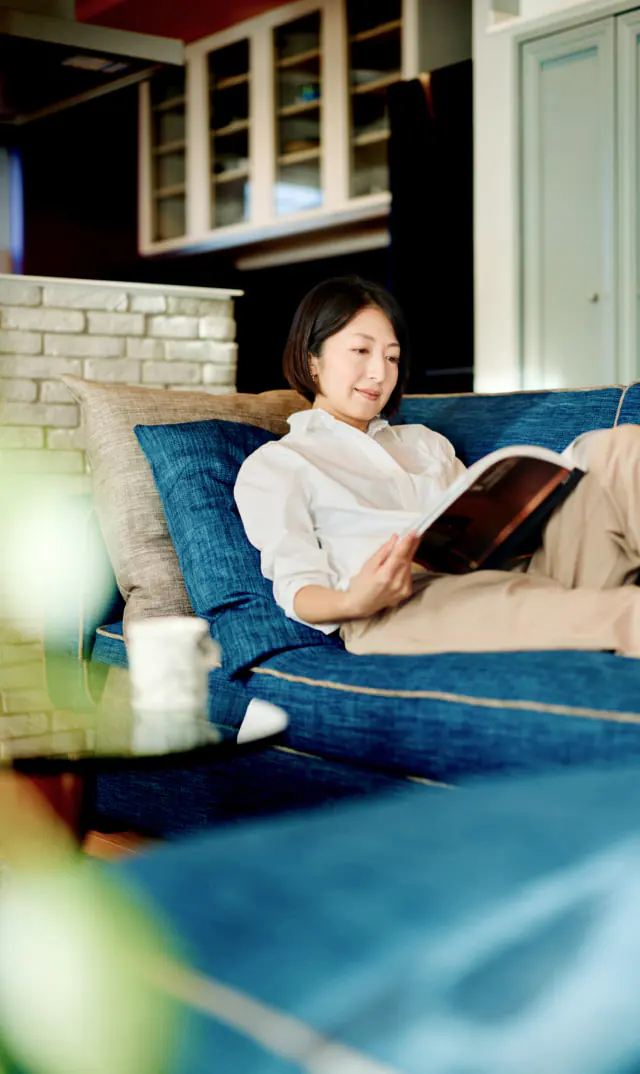青いソファに横になりながら本を読んでいる女性。